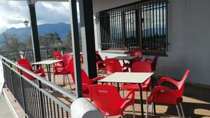 An outdoor seating area with red chairs and white tables, a railing, and a view of mountains. - H&G LOZOYUELA (Lozoyuela-Navas-Sieteiglesias)