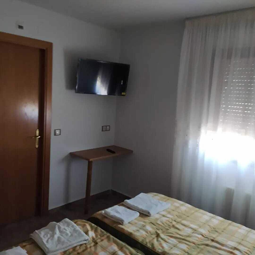 Una habitación de hotel con dos camas, un televisor montado en la pared, un escritorio de madera y una ventana con cortinas.