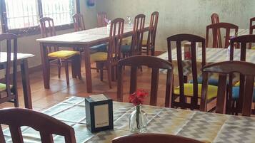 A dining area with multiple tables and chairs, a chandelier, and a potted plant on the wall.