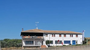 A two-story building with a flat roof, a balcony, and a sign indicating it is a hostel. - H&G LOZOYUELA (Lozoyuela-Navas-Sieteiglesias)