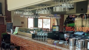 A bar area with a brick counter, multiple stools, hanging glasses, and a visible menu board. - H&G LOZOYUELA (Lozoyuela-Navas-Sieteiglesias)