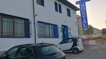 A building with a sign reading "H&G LOZOYUELA HOSTAL". There are two cars parked in front.