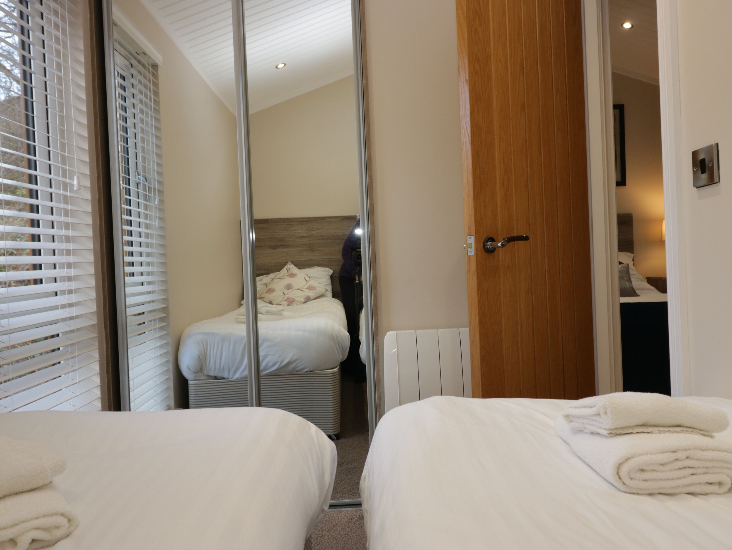 Habitación de hotel con dos camas, una puerta de madera y vista a otra habitación por una puerta de vidrio.