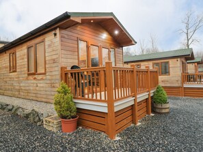 A wooden cabin with a deck, a small potted tree, and a gravel ground. - 8 Woodlands (Ulverston)