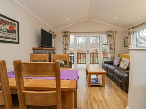 A cozy living room with a wooden dining table, chairs, a sofa, and a television on a stand. - 8 Woodlands (Ulverston)