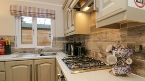 A modern kitchen with a gas stove, a coffee maker, and a dish rack. - 8 Woodlands (Ulverston)