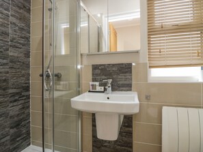 A modern bathroom with a glass shower enclosure, a white sink, and a stone backsplash. - 8 Woodlands (Ulverston)