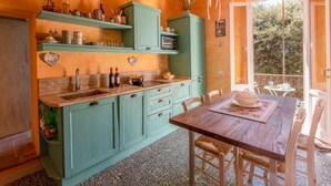 Una cocina con armarios azul verdoso, una mesa de madera y vistas al exterior.