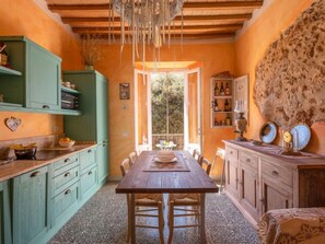 Una cocina acogedora con una mesa y sillas de madera, armarios verdes y suelo de piedra.