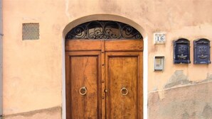 Una doble puerta de madera con un picaporte de metal, ubicada en un arco de entrada, con una placa con el número 16 encima.
