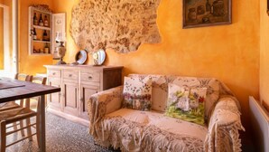 Una habitación acogedora con una mesa de madera, un sofá con cojines estampados, un reloj en la pared y una estantería con botellas.