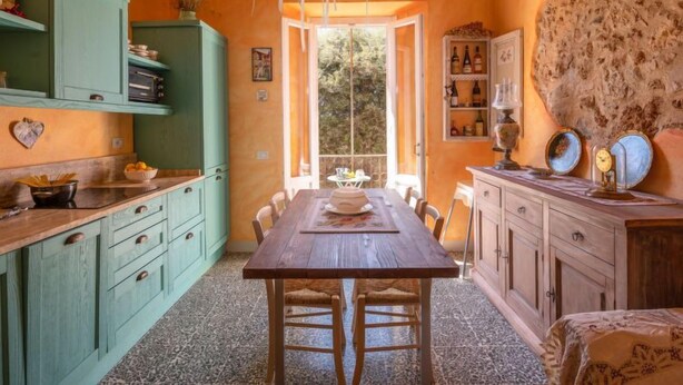 Una cocina acogedora con una mesa y sillas de madera, armarios verdes y suelo de piedra.