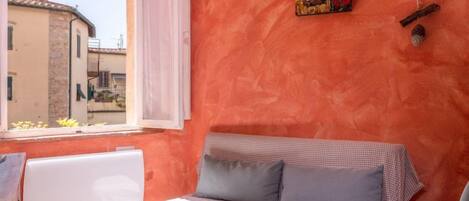 A cozy room with a checkered sofa, a radiator, a window with a view of buildings, and a painting on the wall.