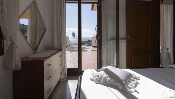 A bedroom with a bed, a dresser, and a sliding glass door leading to a balcony with outdoor furniture. - Apartment Aurora by Interhome (Costarainera)