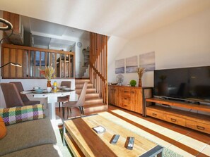 A modern living room with a wooden coffee table, a sofa, and a TV. There is a staircase leading to an upper level.