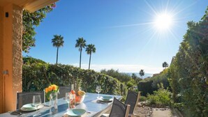 An outdoor dining area with a table set for two, surrounded by lush greenery and palm trees. - Roche Rouge by Interhome (Théoule sur mer)