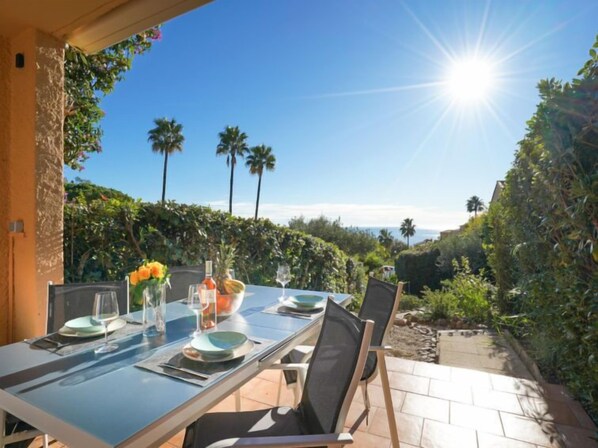 An outdoor dining area with a table set for two, surrounded by lush greenery and palm trees.