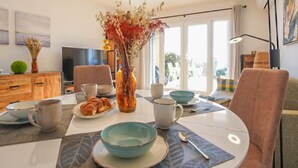 A dining area with a table set for two, a vase with dried flowers, and a television in the background. - Roche Rouge by Interhome (Théoule sur mer)