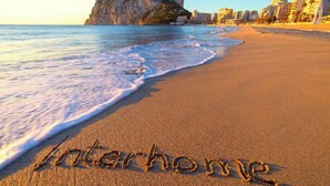 Una platja amb la paraula "interhome" escrita a la sorra, un penya-segat rocos i edificis al fons.
