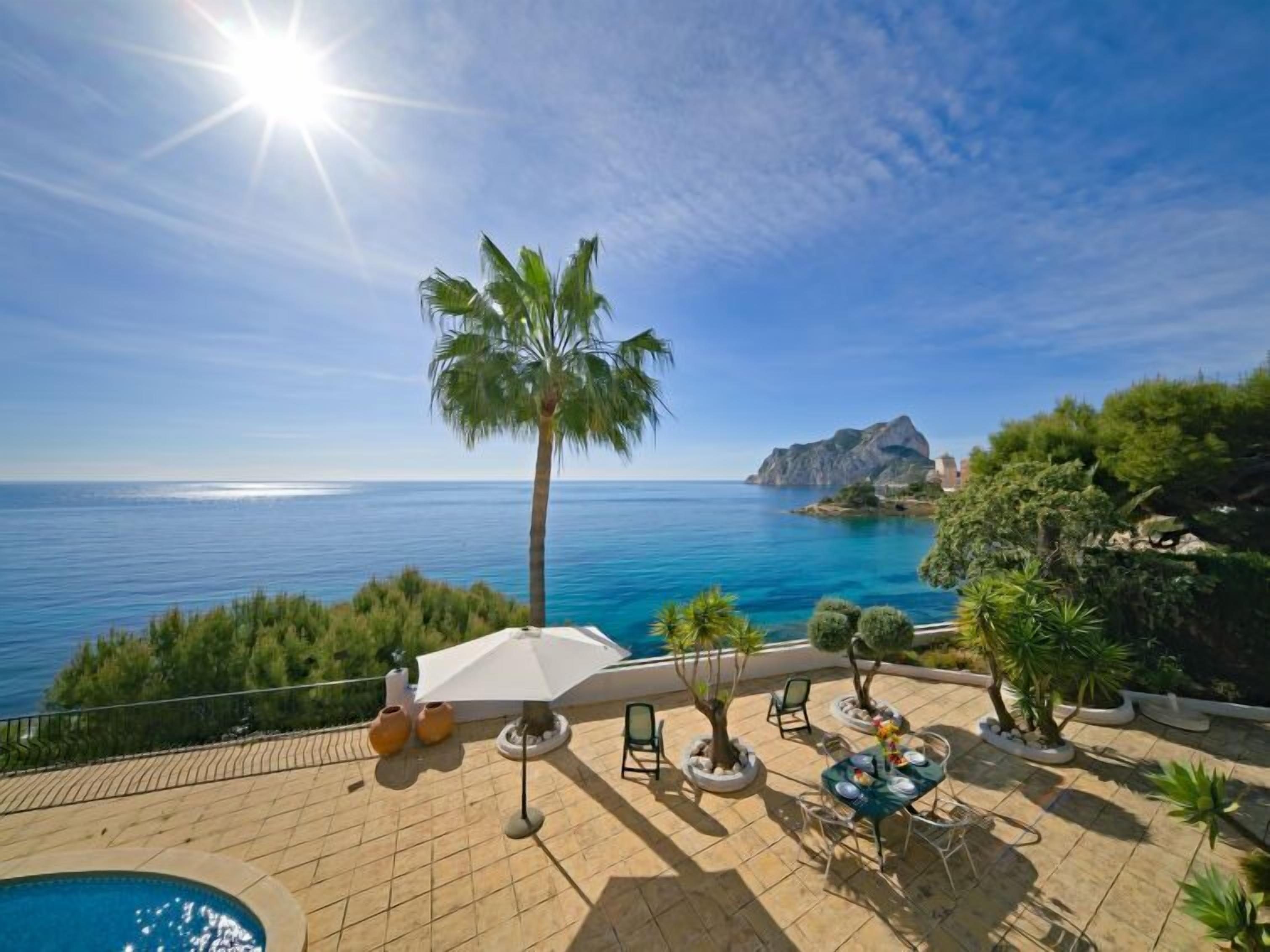 Eine Terrasse mit Pool, Sitzgelegenheiten im Freien und Blick auf Meer und Berge.