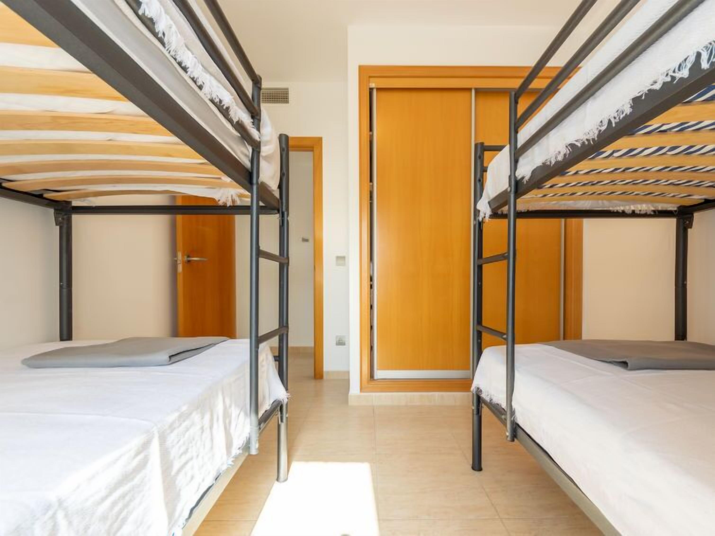 A dormitory room with bunk beds, a wooden door, and a tiled floor.