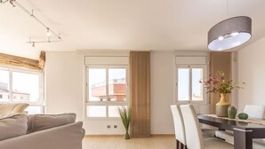 A modern living room with a sofa, dining table, chairs, and a vase with flowers. - Apartment Star by Interhome (L'Ampolla)