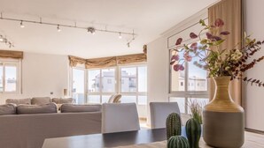 A modern living room with a sofa set, a dining table with a vase of flowers, and a large window with curtains. - Apartment Star by Interhome (L'Ampolla)