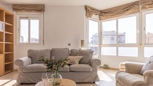 A living room with a beige sofa, a round coffee table with a vase and glasses, and large windows with curtains. - Apartment Star by Interhome (L'Ampolla)