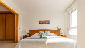 A bedroom with a bed, nightstands, a window, and a door. - Apartment Star by Interhome (L'Ampolla)