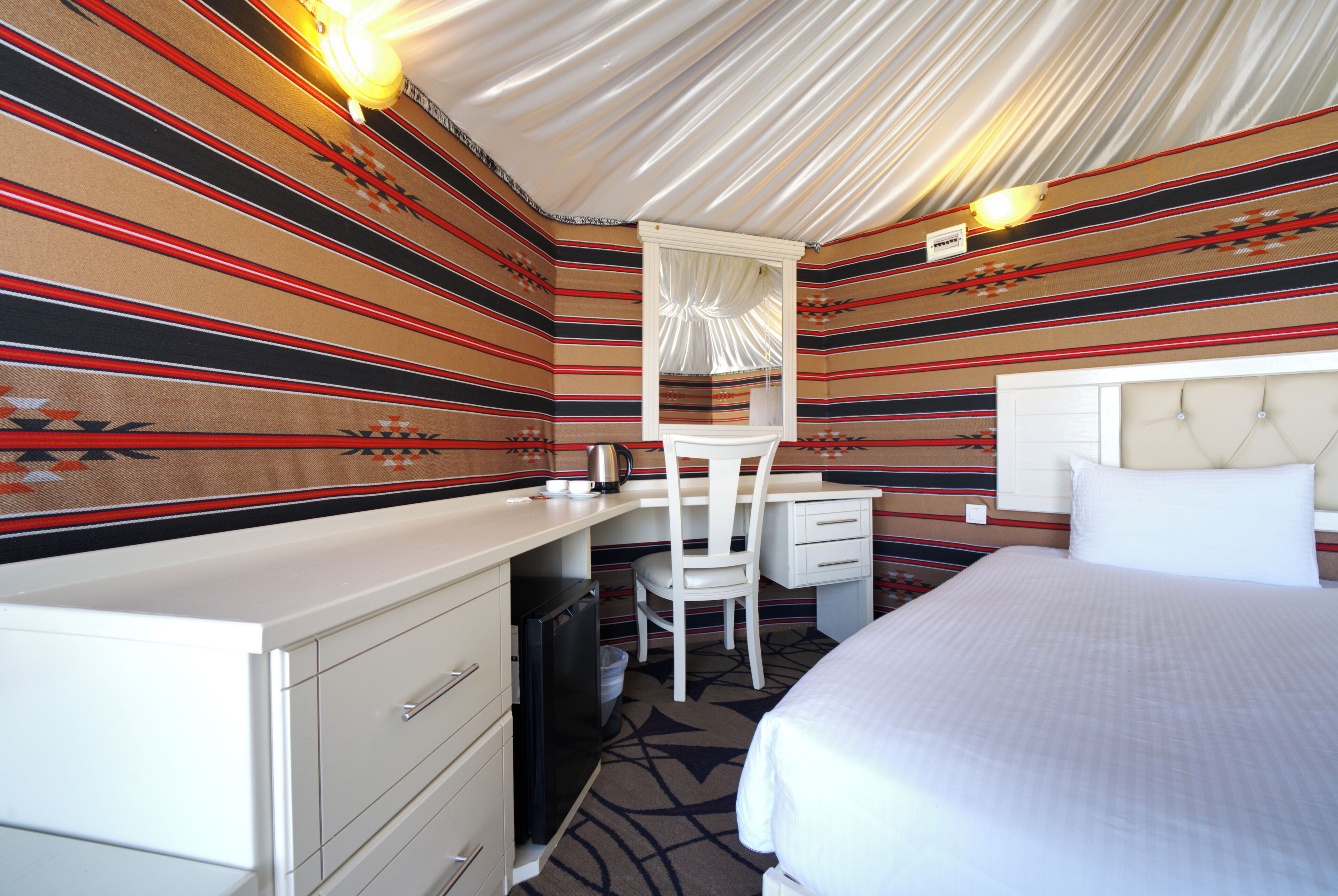 A hotel room with a bed, a desk, a chair, and a minibar.