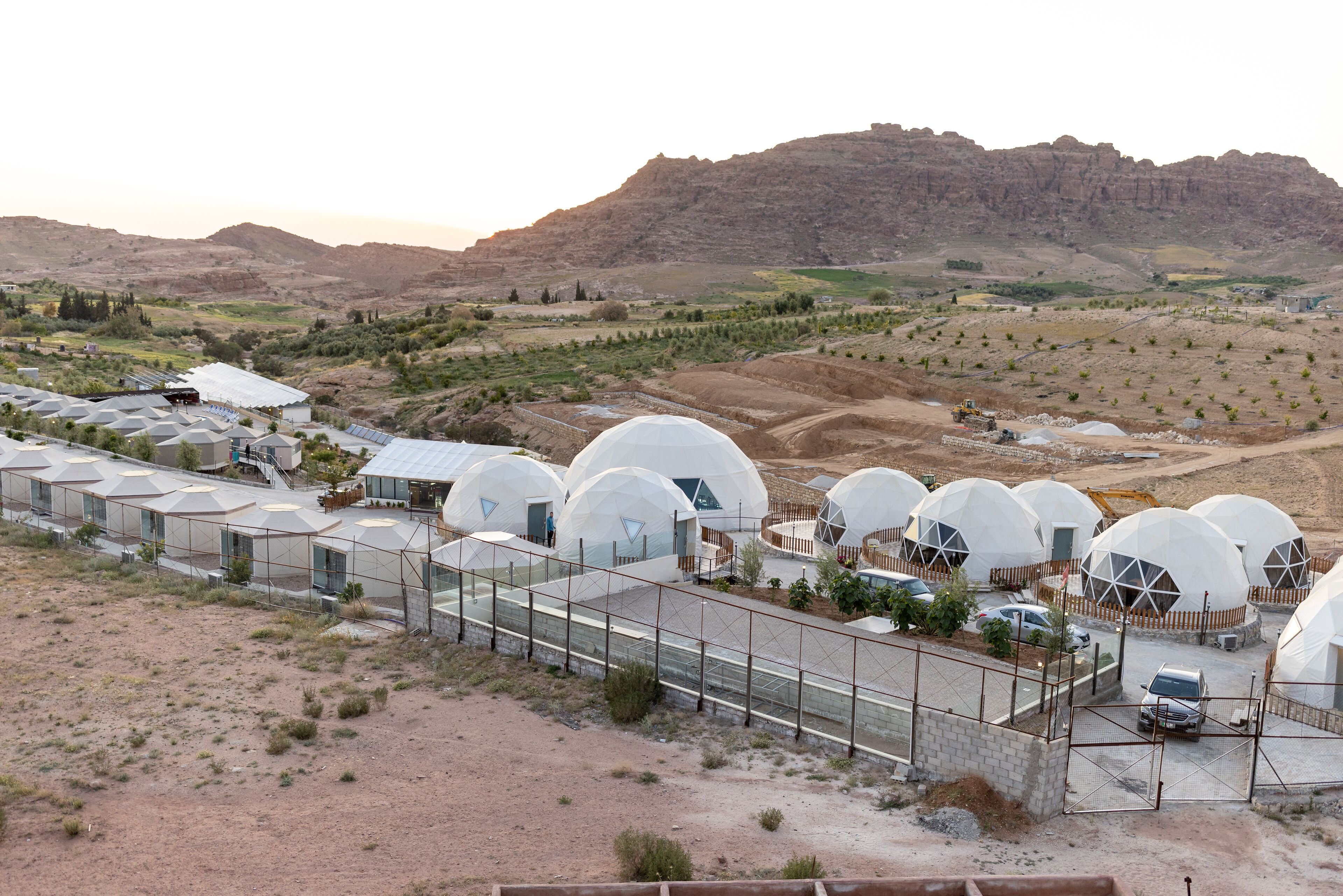 Une série de structures en forme de dôme, entourées d’une clôture, se dressant sur un fond de paysage montagneux.