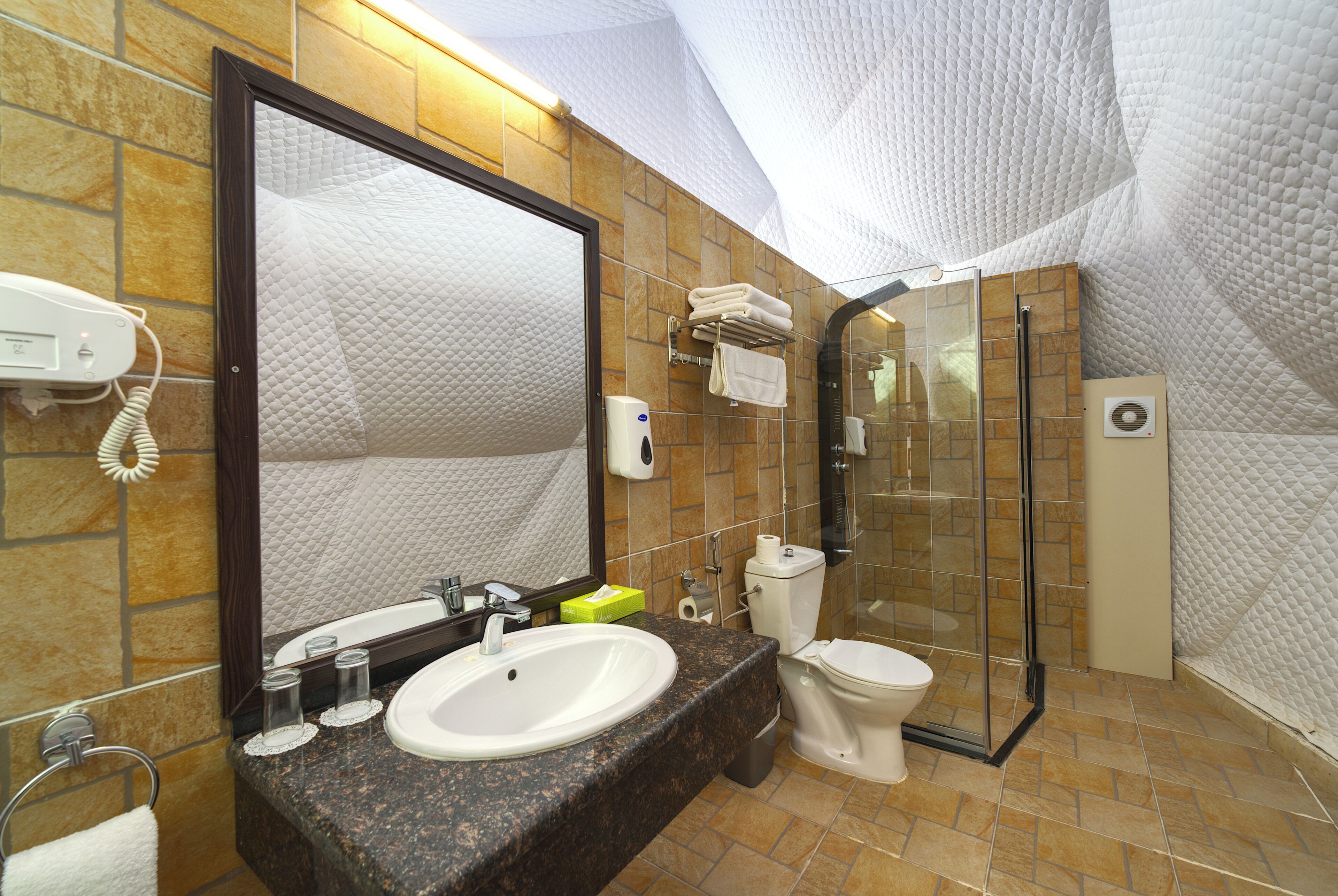 Un baño con encimera de granito, un lavamanos blanco, un espejo grande, un inodoro y una cabina de ducha con paredes de vidrio.