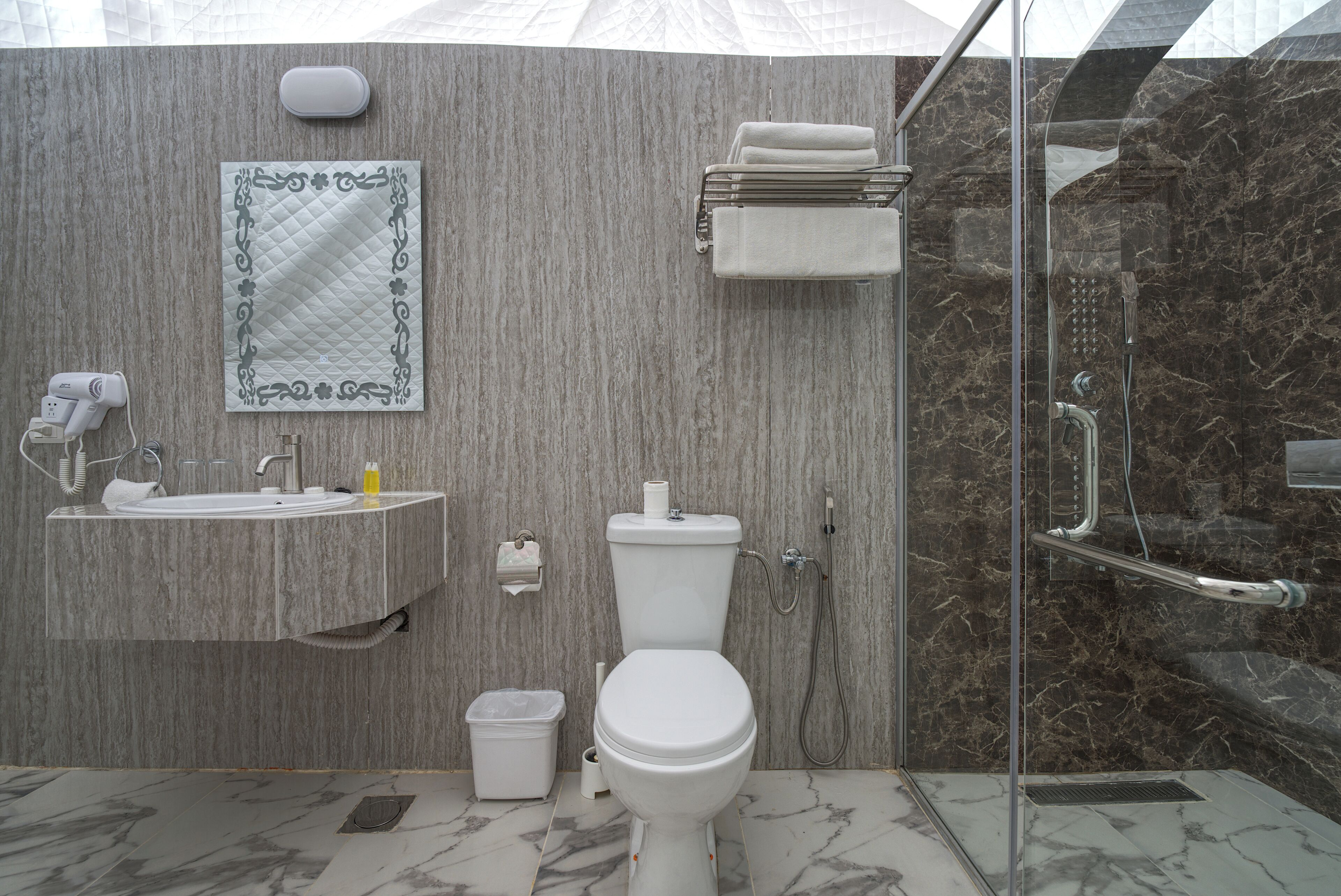 A modern bathroom with a marble floor, a toilet, a sink, and a shower area.