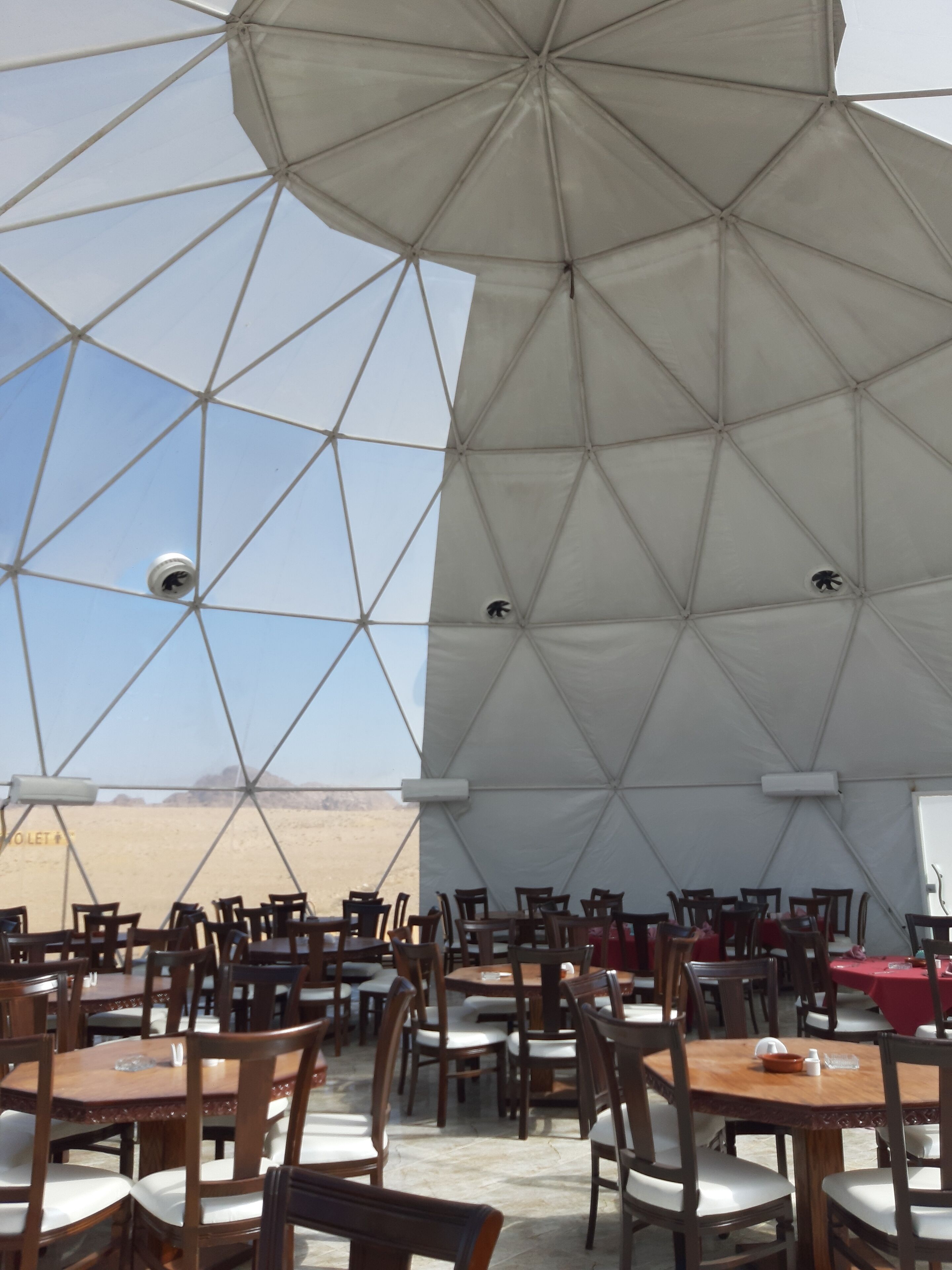 A dining area with tables and chairs under a large tent with a geometric pattern.