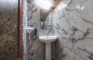 Un baño con lavamanos pedestal blanco, paredes de mármol y espejo con motivos decorativos.