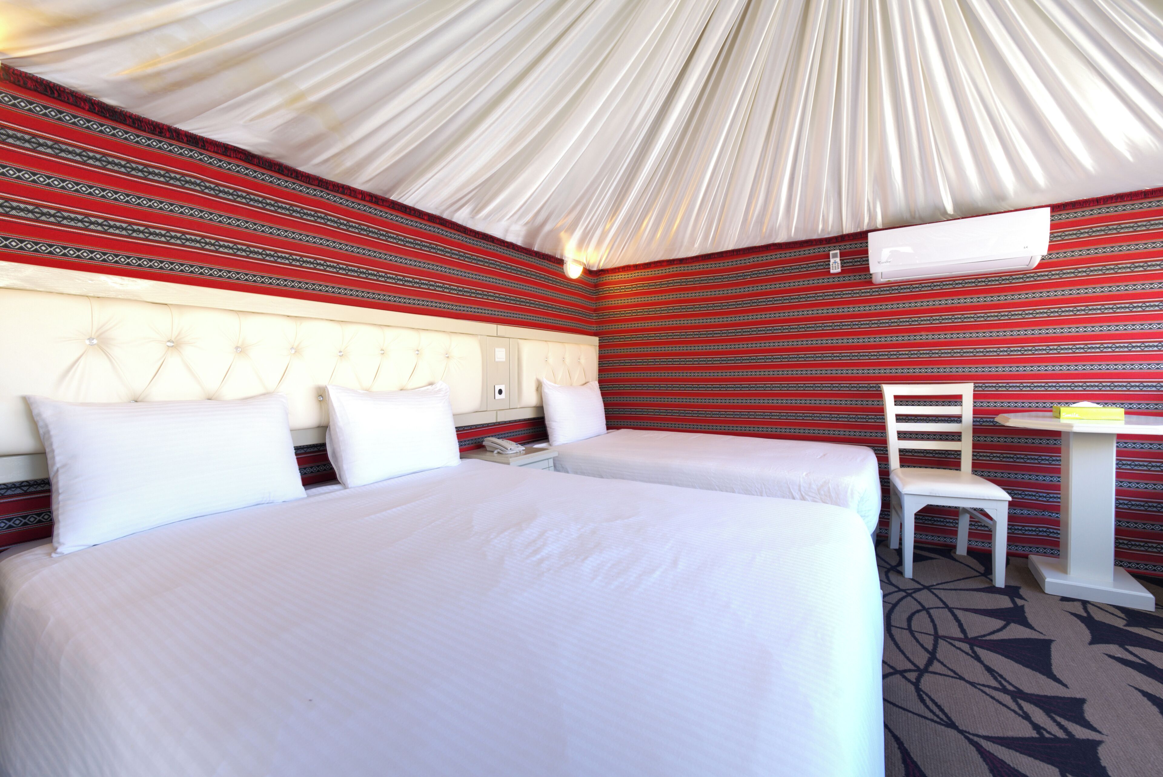 Habitación de hotel con dos camas, una silla, una mesa y una pared con rayas rojas.