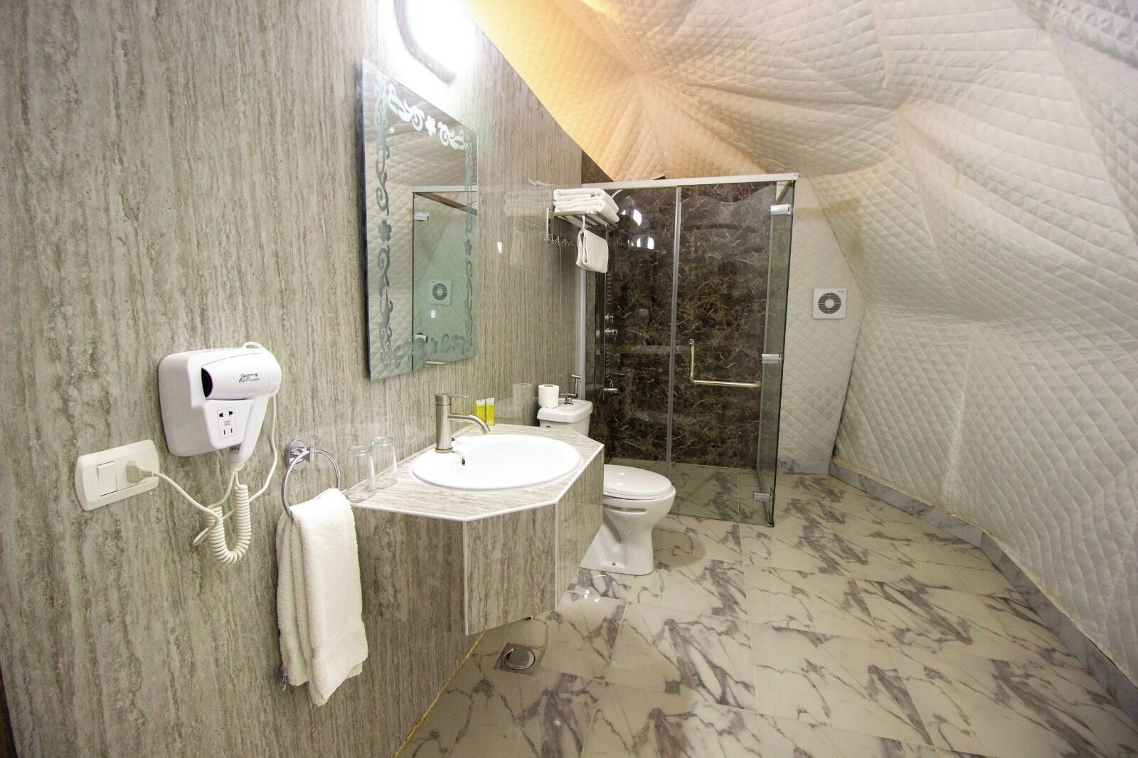 A bathroom with a marble floor, a sink, a toilet, a shower, and a hairdryer on the wall.