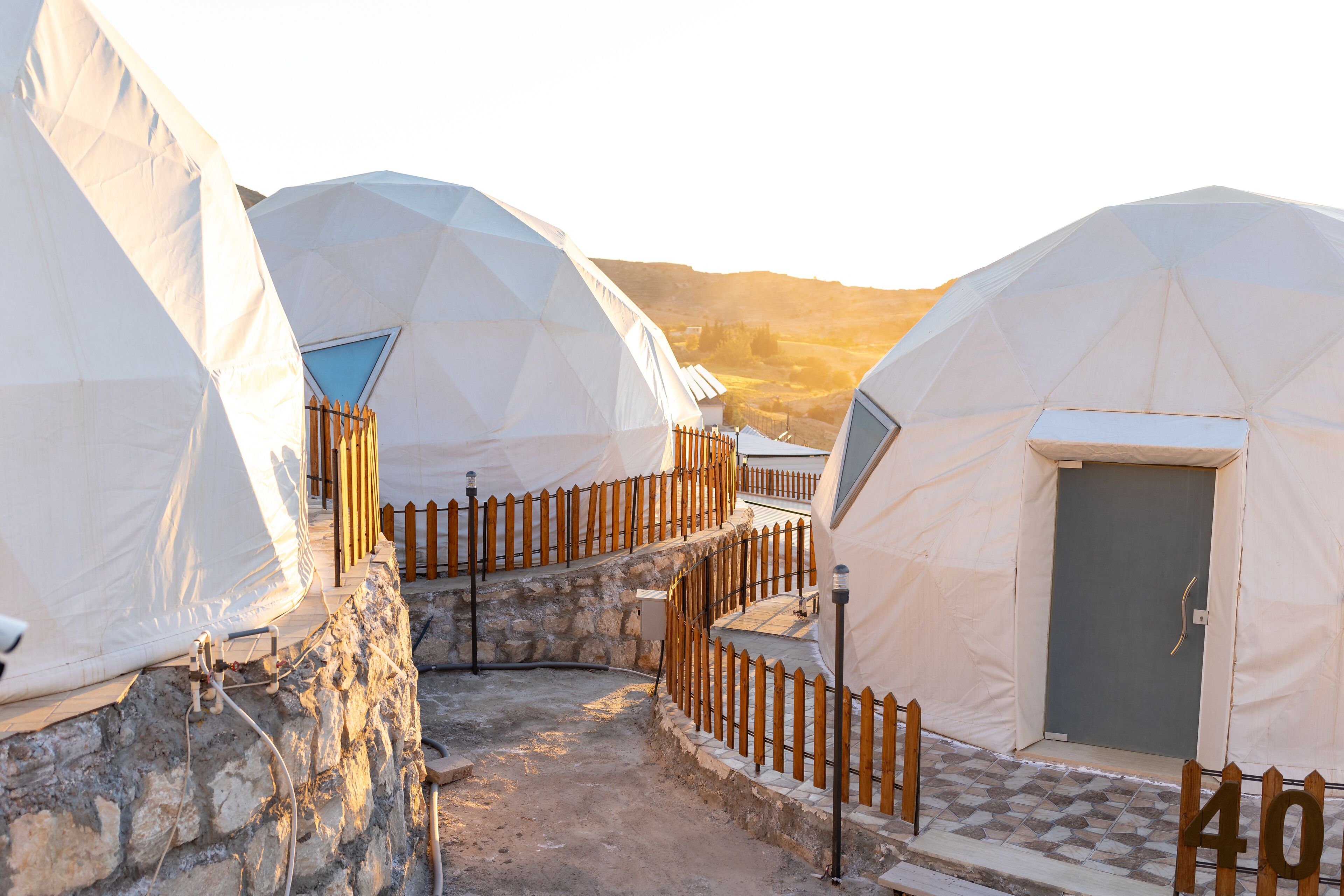 A series of dome-shaped tents with a stone wall and wooden fence, connected by a pathway.
