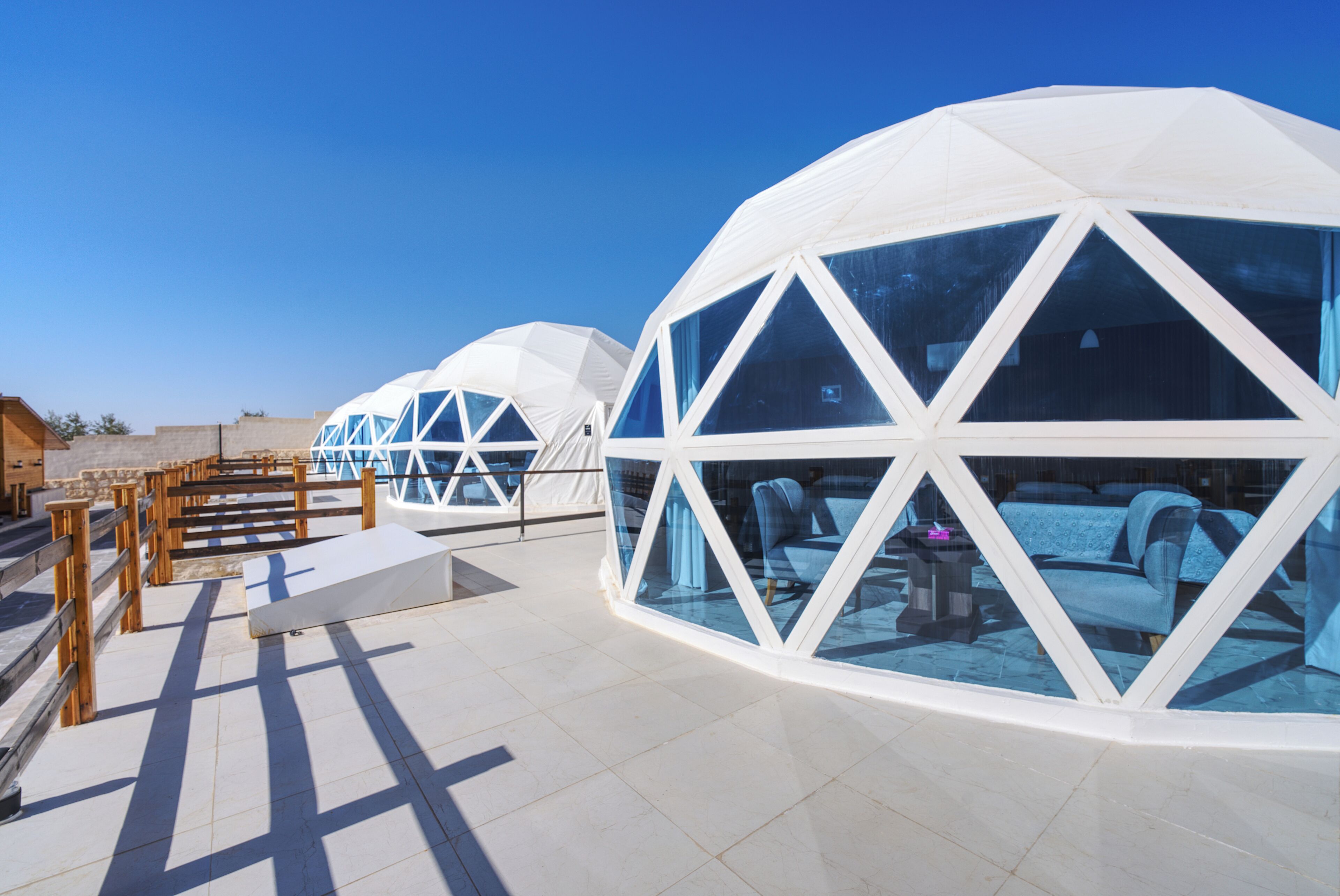 A series of geodesic dome structures with transparent walls, wooden railings, and a tiled floor.