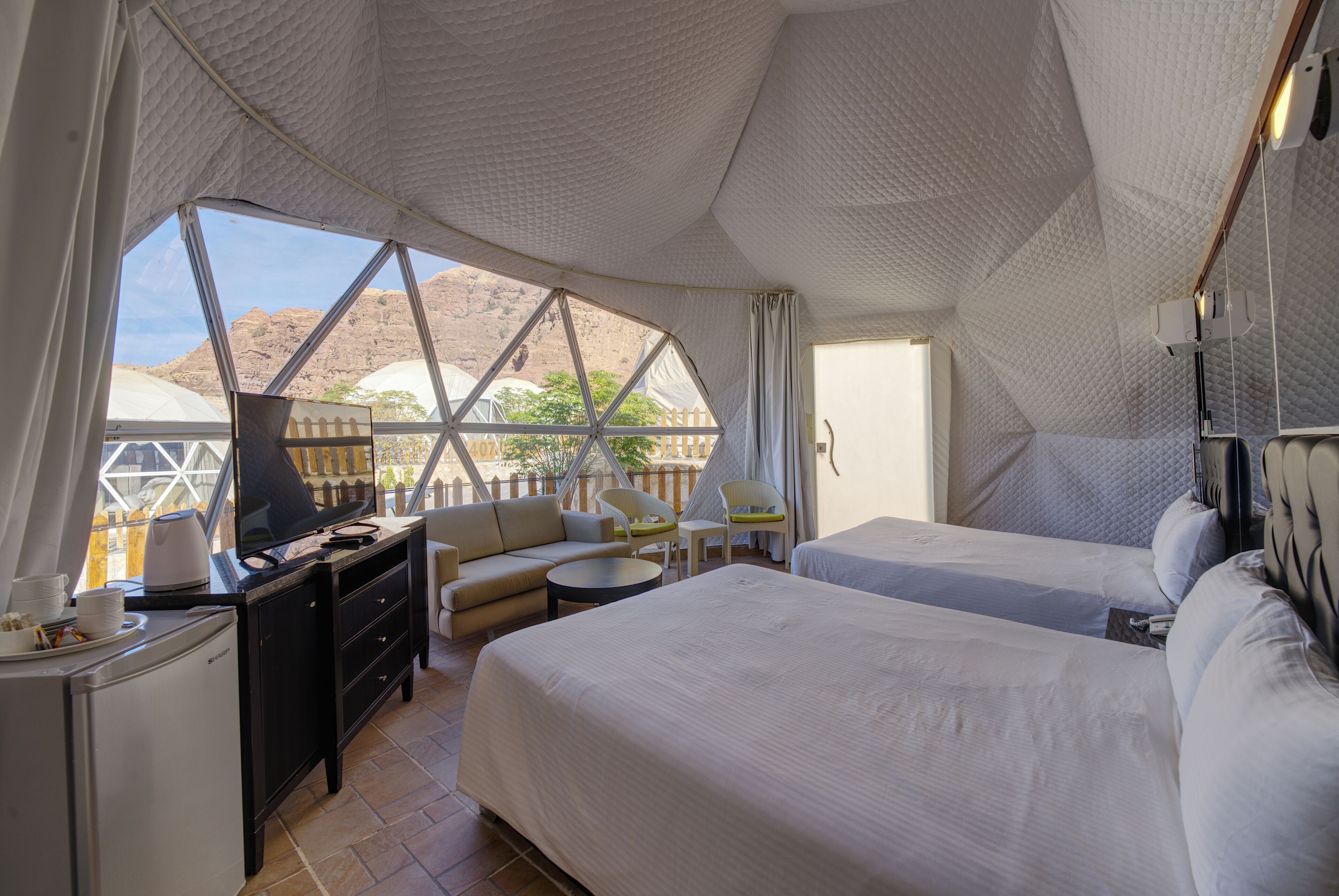 A tented accommodation with two beds, a desk, and a seating area.
