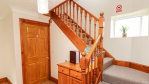 A wooden staircase with a banister, a closed wooden door, and a window with a plant. - Adeline (Burry Port)