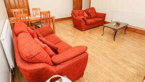 A living room with a red sofa, a red armchair, a wooden dining table with chairs, and a small coffee table. - Adeline (Burry Port)