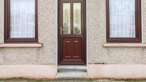 A two-story building with a central entrance door, flanked by two windows with decorative glass panes. - Adeline (Burry Port)