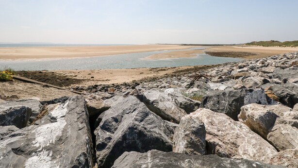 A rocky shoreline with a sandy beach and calm water. - Adeline (Burry Port)