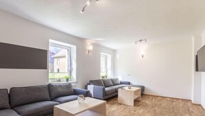 A modern living room with a grey sectional sofa, a wooden coffee table, and a grey sofa. There are two windows providing natural light, and the room has a wooden floor. - mit 3 Schlafzimmern by Interhome (Eisenerz)