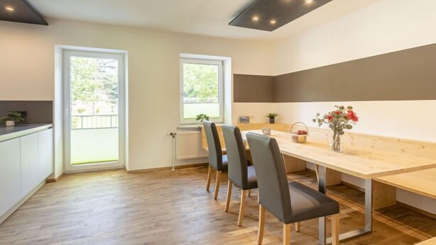 A modern kitchen with a wooden table and chairs, large windows, and a view of greenery outside. - mit 3 Schlafzimmern by Interhome (Eisenerz)