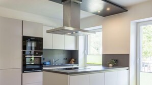 A modern kitchen with white cabinetry, a central island, and a large window providing natural light. - mit 3 Schlafzimmern by Interhome (Eisenerz)