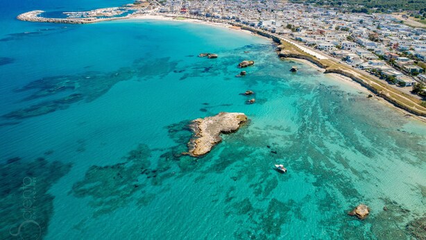 An aerial view of a coastal town with clear turquoise waters, a sandy beach, and a dense cluster of buildings along the shore. - 3231 Villino San Basilio by Barbarhouse (Melendugno)