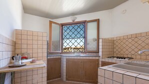 A kitchen with wooden cabinets, a gas stove, a sink, and a window with a view. - 3231 Villino San Basilio by Barbarhouse (Melendugno)