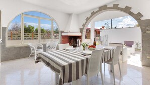 A dining area with a large table, white chairs, and a brick oven. - 3231 Villino San Basilio by Barbarhouse (Melendugno)